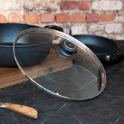 Tempered 12.5" Glass Lid tilted on side of pan on cutting board and kitchen counter top